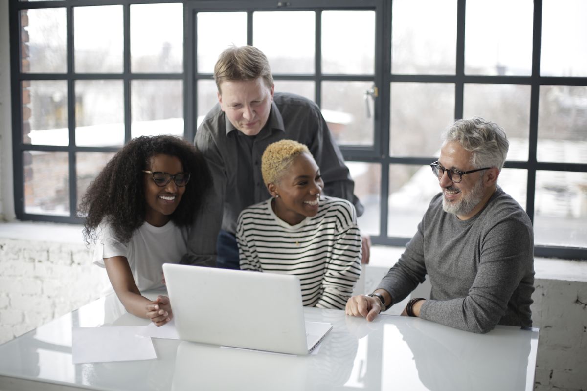 Four colleagues collaborating happily around a laptop by a sunlit window