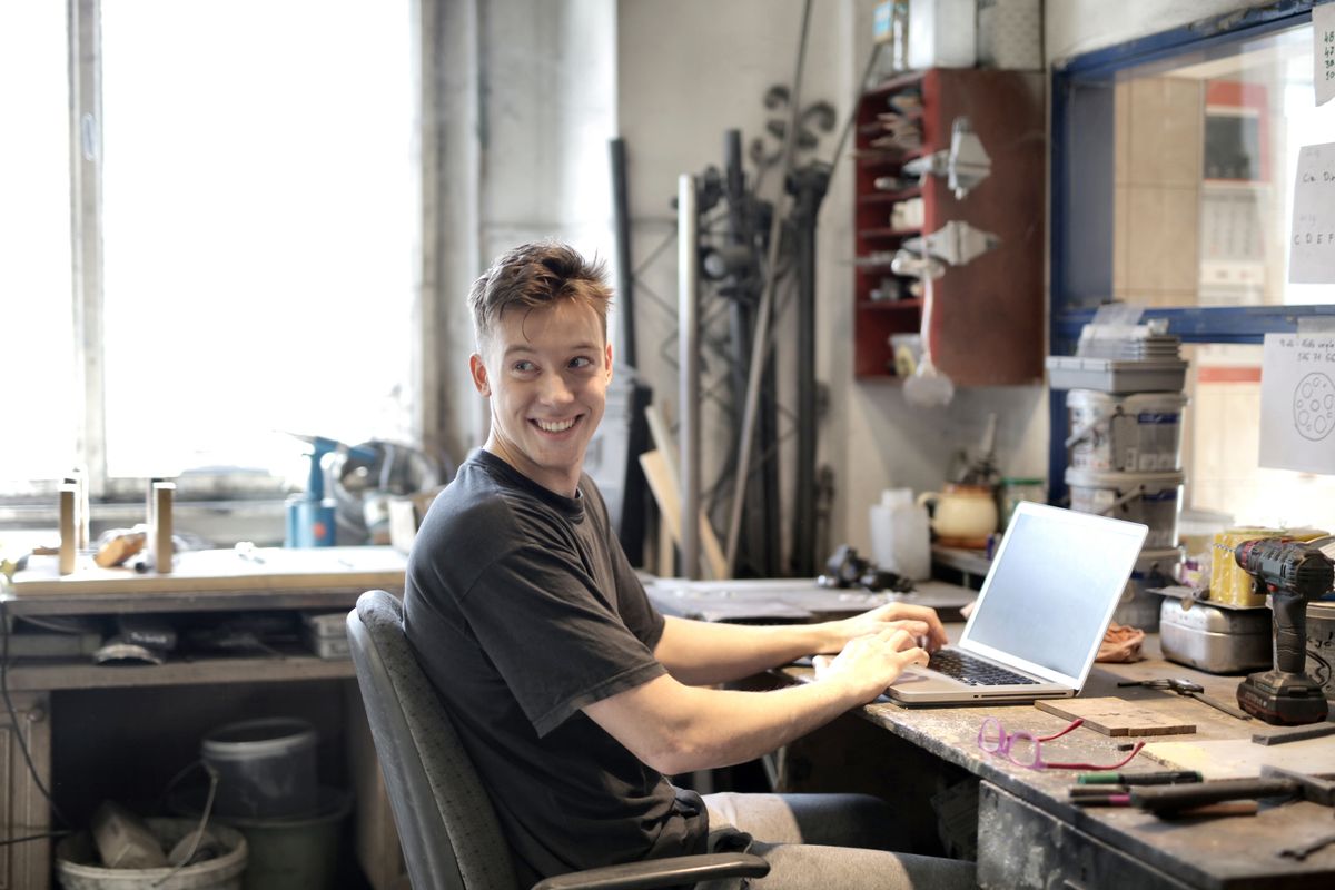 A smiling small business owner working on a laptop at their workbench